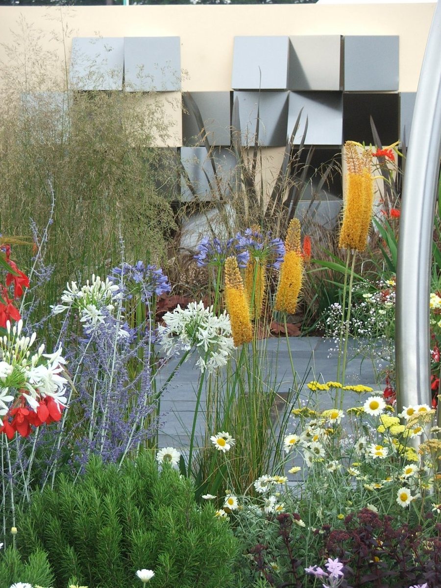 Folded stainless steel wall panels mounted proud of a rendered wall behind planting